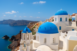 Witte huizen en blauwe koepels op Santorini met uitzicht op de Egeïsche Zee en omliggende Cycladische eilanden onder een heldere hemel.