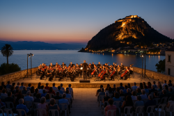 Orkest speelt bij zonsondergang in Nafplio met publiek en vestingmuur op achtergrond