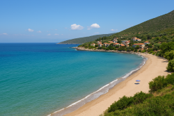 Uitzicht op een rustige baai aan de oostkust van de Peloponnesos met turquoise zee, zandstrand en een dorp op de heuvel.