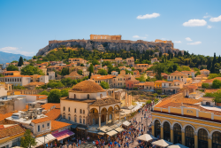 Panoramisch uitzicht over Athene met de Akropolis en het Parthenon centraal, omringd door historische gebouwen, moderne stadswijken en een heldere blauwe lucht.