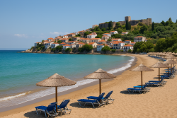 Koroni strand met rieten parasols en ligstoelen langs een goudkleurig zandstrand, turquoise zee en witte huizen onder een historische vesting.